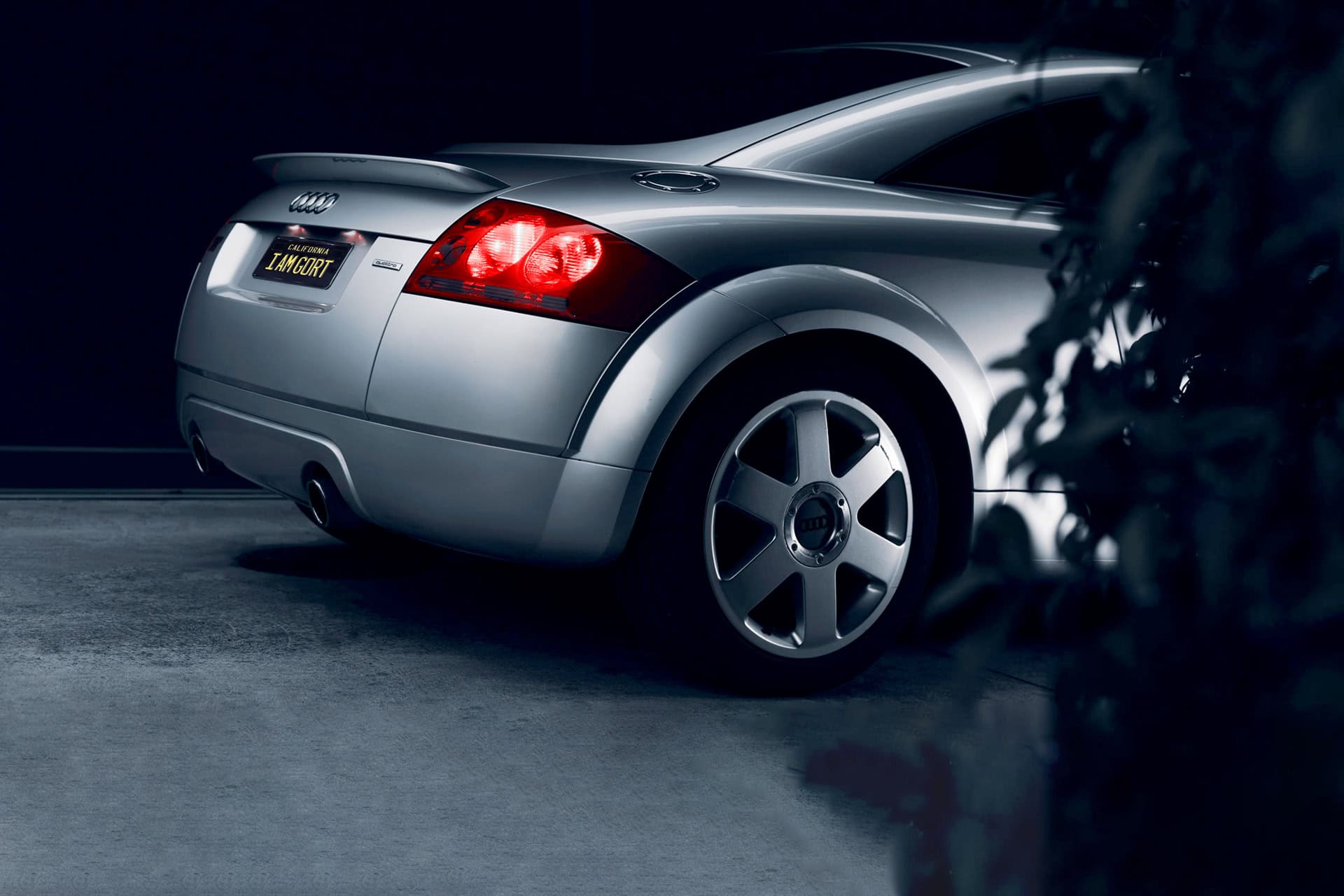A sleek silver Audi sports car at night with a custom "I AM GORT" license plate, highlighted by stylish lighting and a modern design emphasizing luxury and automotive excellence.