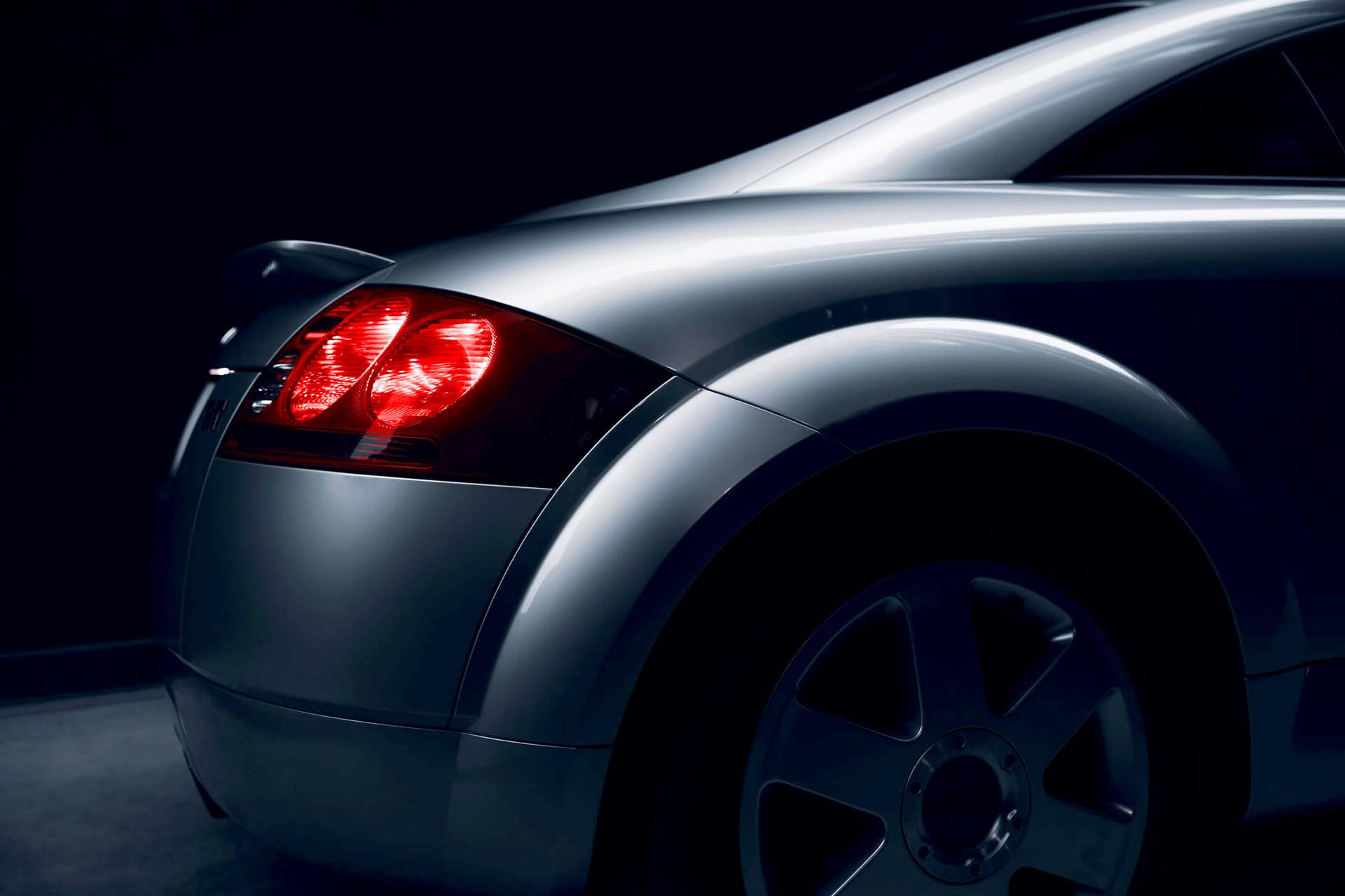 Sleek silver sports car with illuminated taillights against a dark background, showcasing premium automotive design and luxury vehicle aesthetics.
