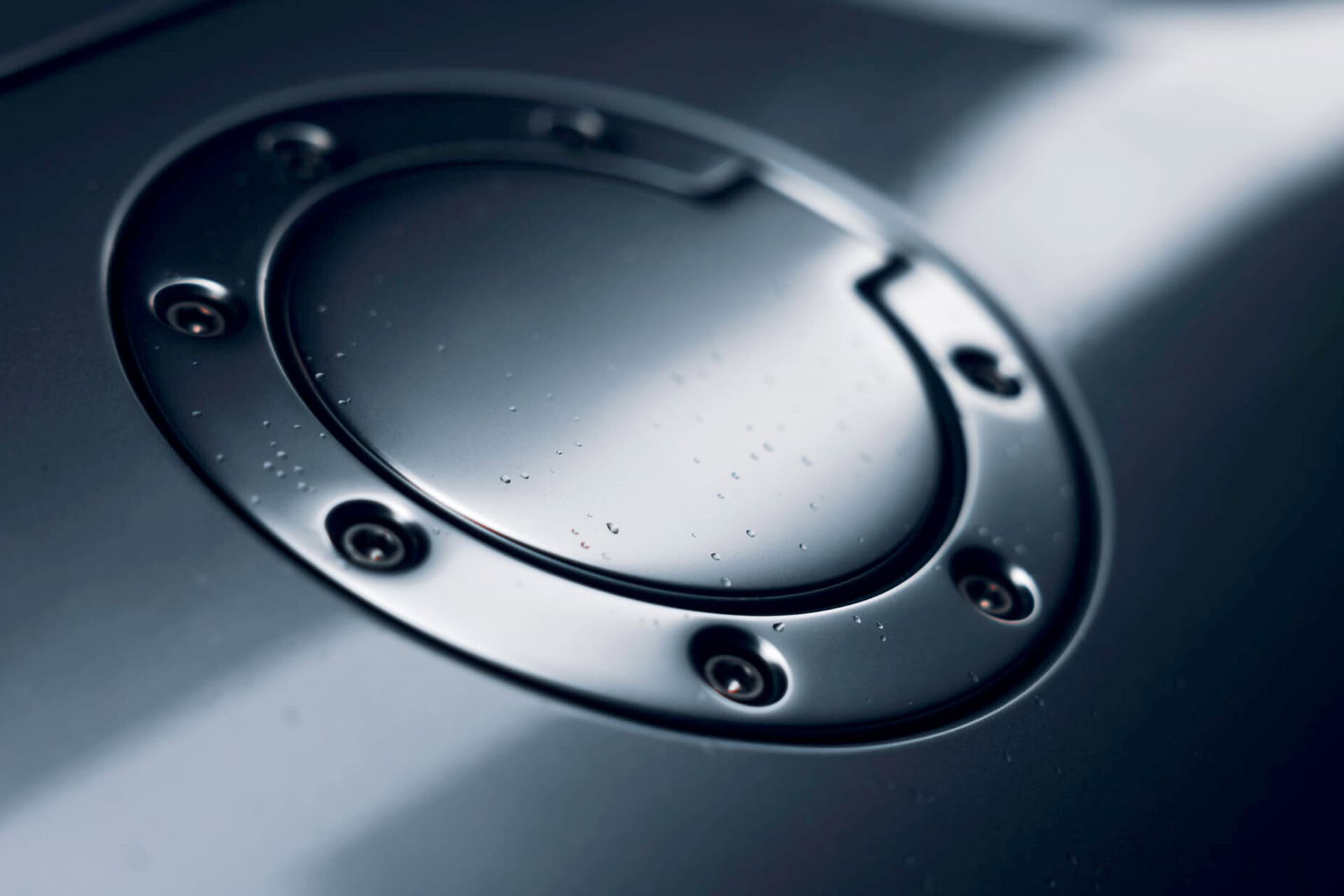 Shiny metallic surface with a circular vent or speaker, close-up detail highlighting smooth, modern industrial design elements.