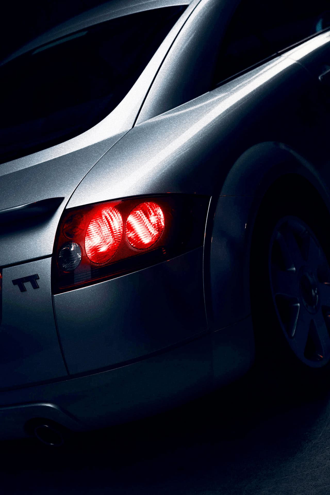 Silver sports car rear close-up highlighting sleek aerodynamic design and illuminated taillights.