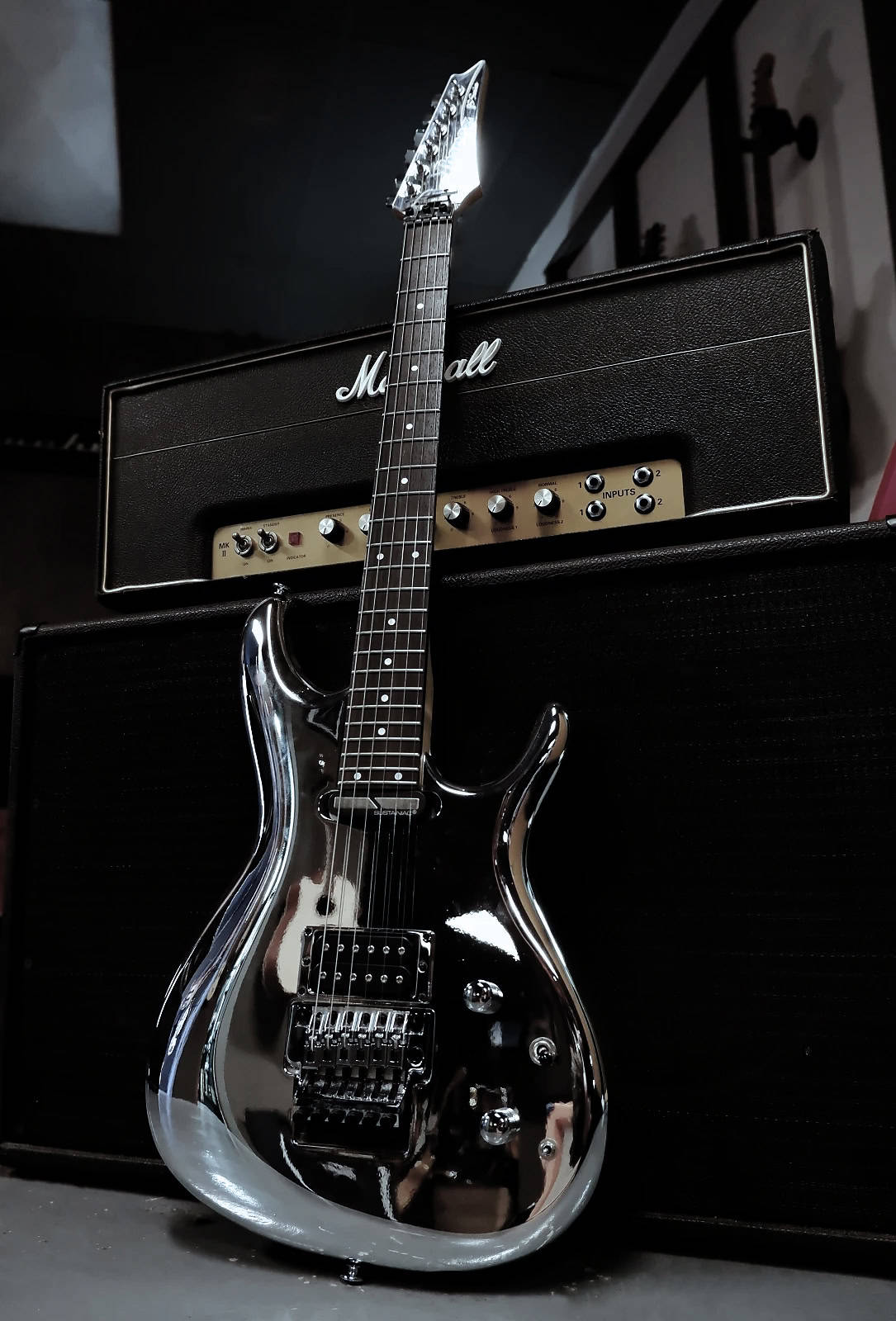 Shiny black electric guitar leaning against a Marshall amplifier with a dark background.